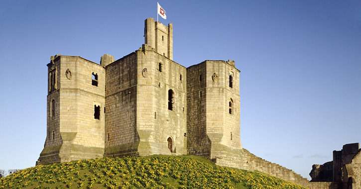 View of Warkworth Castle, Northumberland, on a hill with flowers, in background blue sky